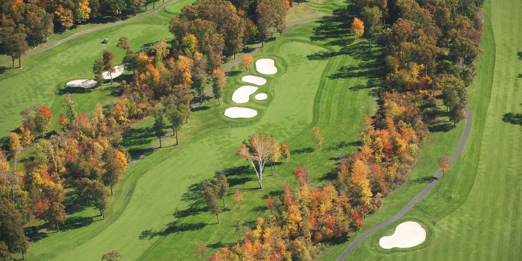 Aerial view of a tree-lined golf fairway and green with sand bunkers in vivid autumn foliage. iStock photo, credit: Willard.